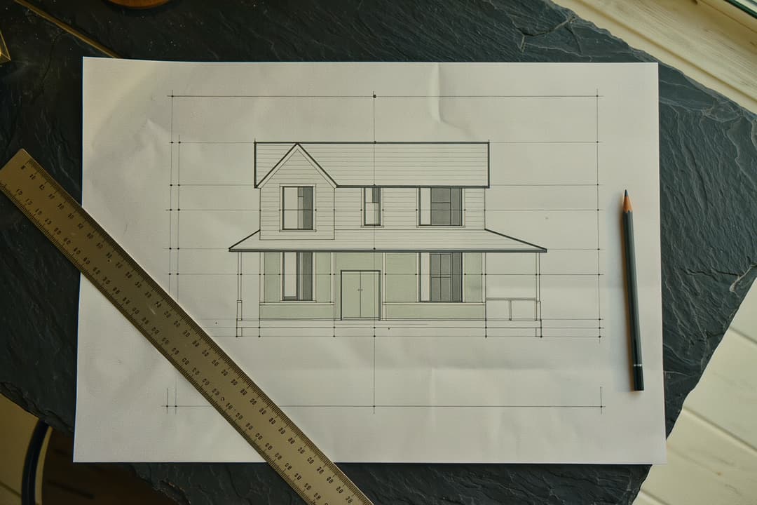 An architectural drawing of a two-storey house held flat by a ruler and pencil